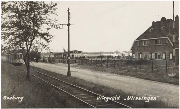 Vliegveld Souburg gezien vanaf de Nieuwe Vlissingseweg. Van
    links naar rechts: de tram, het KLM-gebouw, een DC3 vliegtuig en het stationsgebouw.